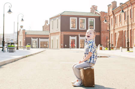 little boy sitting on vintage suitcase on the sunny deserted street in the morningの写真素材