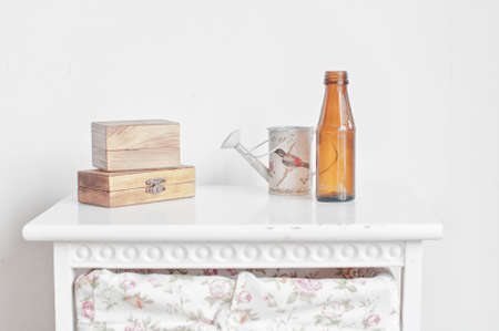 Two wooden boxes, bottle and vintage watering can on the white bedside tableの写真素材