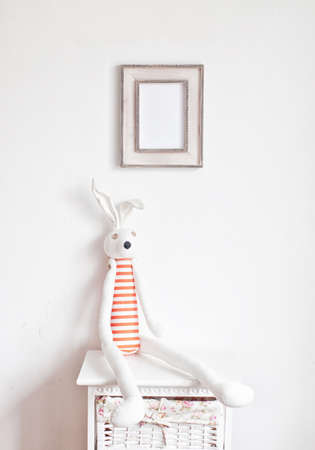 Striped bunny sitting on the bedside table and picture frame on the white wallの写真素材