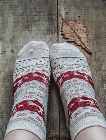 Feet in knitted woolen warm socks and dry yellow oak leaf on wooden backgroundの写真素材