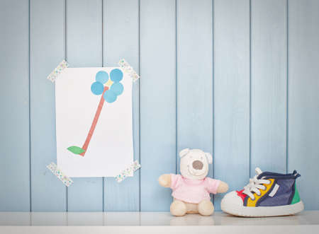 Funny colorful child picture on the wall in the room, tiny baby shoes and teddy bear toyの写真素材