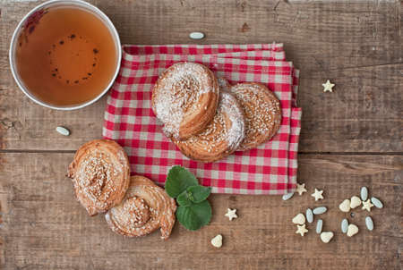 Festive sweets, puff cookies with sesame seeds, sugar candies and cup of tea on gingham table clothの写真素材