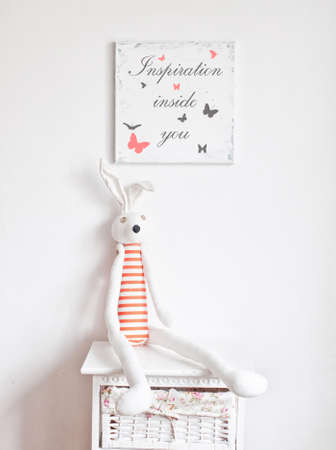 Striped bunny sitting on the bedside table and picture frame on the white wallの写真素材