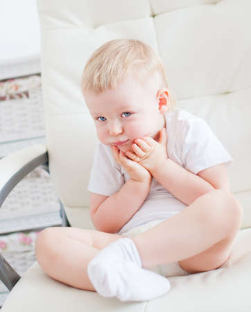Cute little boy is sitting on the white chair in baby roomの写真素材