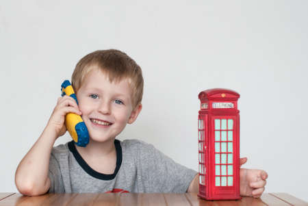 Little cheerful boy talking on the phone and vintage british red telephone boothの写真素材