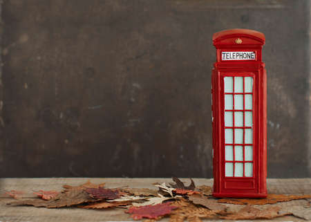 Autumnal image with dry maple leaves and red british vintage phone boothの写真素材