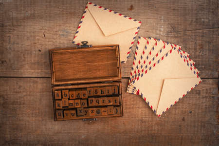 wooden stamps alphabet in old vintage box and ancient envelopes on autumnal dry maple leaves backgroundの写真素材