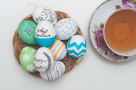 Easter  decorated eggs in a straw plate and english tea on white backgroundの写真素材