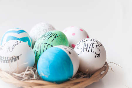 Easter  decorated eggs in a straw plate on white backgroundの写真素材