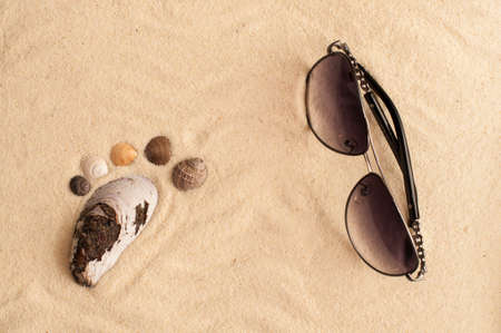 sea shells footprint and sunglasses on a sandy beachの写真素材