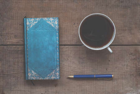 mug of hot coffee, notebook and pen on vintage wooden desktopの写真素材