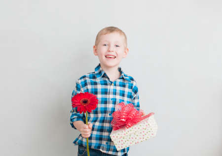 Cheerful little boy with red flower and gift