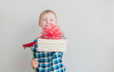 Cheerful little boy with red flower and gift box