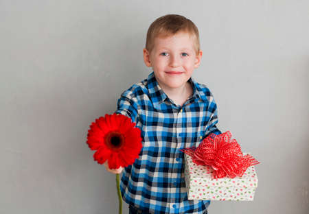Cheerful little boy with red flower and gift box