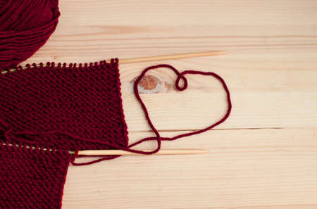 Woolen burgundy yarn knitting on wooden tableの写真素材