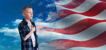 Proud patriotic kid holding his hand on his heart and looks at american flagの写真素材