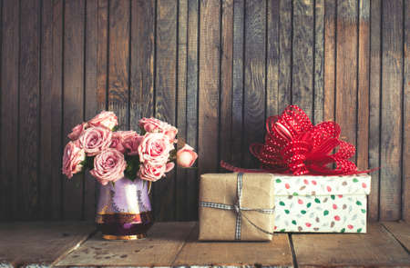 Beautiful pink roses in a vintage jug and gift boxes on rustic wooden background
