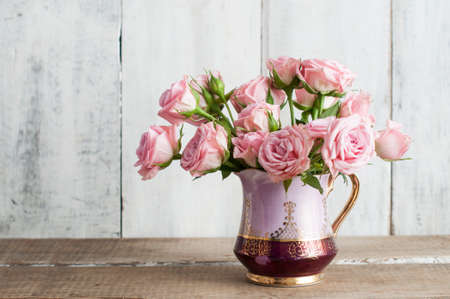 Pink roses in vintage jug on white rustic wooden tableの写真素材