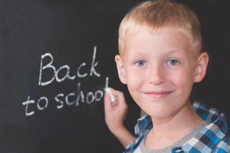 Smiling kid writing words BACK TO SCHOOL with chalk on the blackboardの写真素材