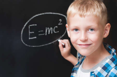 Boy writing formula of energy on the blackboard in classroomの写真素材