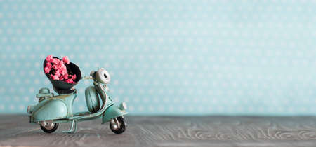 Tiny vintage toy blue mototrcycle with bunch of pink flowers on wooden table in nursery room