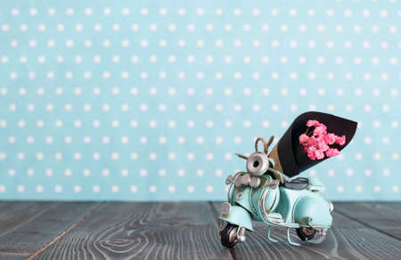 Vintage toy blue mototrcycle with bunch of pink flowers on wooden table in nursery room