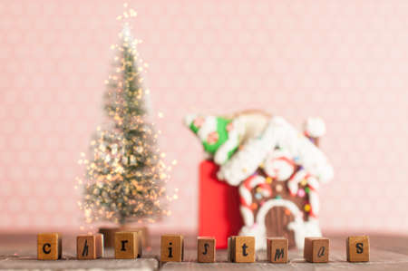 Christmas evergreen tree with lights, gingerbread house, word christmas and gifts on the table in pink nursery roomの写真素材