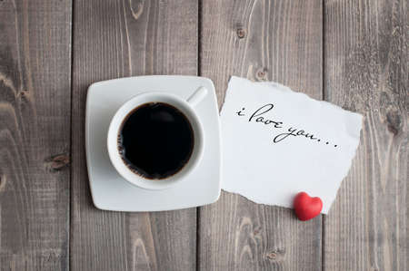 Cup of black coffee and love Valentine's day message with red heart shape on rustic woodenの写真素材