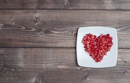 Red pomegranate seeds in shape of heart in a dish on wooden kitchen tableの写真素材