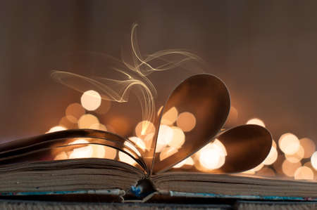 An open book with pages curved in shape of heart and bokeh lightの写真素材