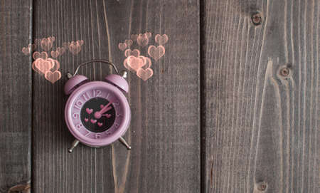 It's love o'clock. Valentine's pink alarm with heart shaped symbols on woodenの写真素材