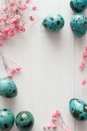 Easter quail eggs with flowers on white wooden background