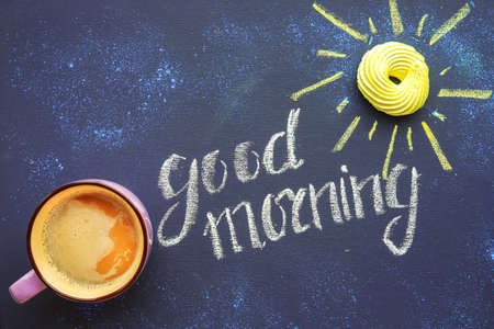 Morning composition of coffee and donut as a sun on chalkboard, inscription "good morning" written with chalkの写真素材