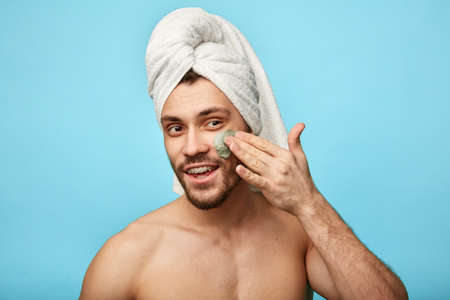 positive guy using cream after taking a shower isolated over blue background, studio shot.cosmetology, cosmetic concepts. happinessの写真素材