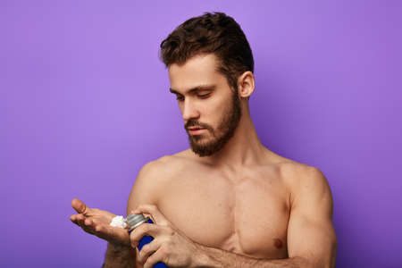 Young serious handsome man is ready to shave his beard.He is holding foam in his palm. close up portrait, isolated on the blue background.studio shot.の写真素材