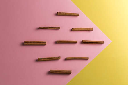 rhombus shaped composition of raw sinnamon sticks isolated on the pink and yellow backgroundの写真素材