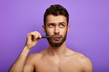 pensive thoughtful sexy guy looking aside and brushing his teeth. lifestyle, free time, pastime conceptsの写真素材