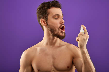 naked guy using mouth freshner. medicine, business concept. man having problems with breath. spray for throat. guy treating his throat with spray.の写真素材