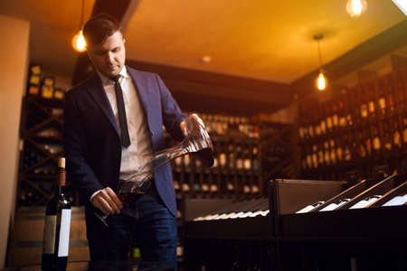 stylish young man in blue suit and white shirt pouring wine from decanter to the glass. close up photo.copy space. passion for wineの写真素材