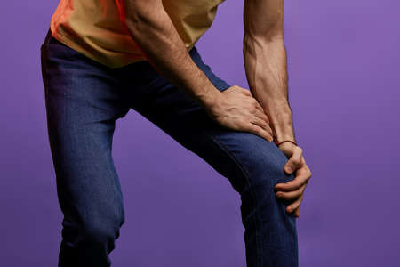 young man suffering from pain n blue background. close up cropped photo.guy has broken his leg
