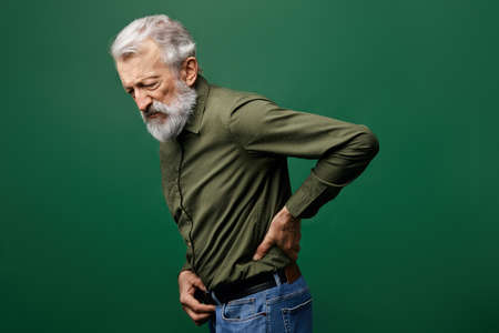 old man suffering from referred pain in the back. weakness concept. shooting, piercing pain in back. close up side view photo.の写真素材