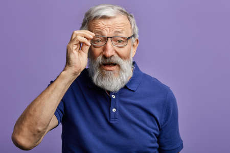 cheerful old man looking through the glasses at the camera isolated on blue background. close up...