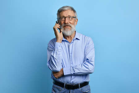 handsome senior man looking up, talking on mobile phone isolated against sky blue background. old...
