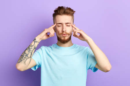 Young relaxed man concentrating on thoughts,suffering from headache, pressing fingers to temples,...