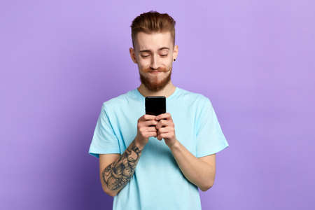 Happy stylish funny good looking man typing sms on blue background. close up portrait. isolated blue background. studio shot.の写真素材