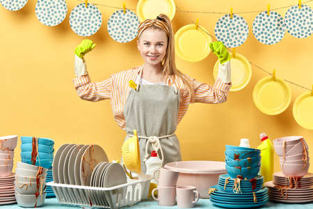cheerful blonde housewife in gray apron in green gloves showing biceps isolated on yellow background. close up portrait. happiness, the winner of contest.の写真素材