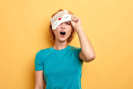 blond young tired woman wearing sleeping mask after awakening isolated over yellow background. close up portrait. tiredness, feeling , emotion. difficult mondayの写真素材