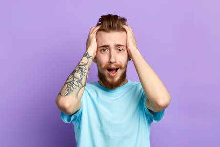 Portrait of a frightened bearded man with palms on his head and screaming isolated over blue background. close up portrait.emotion and feelingの写真素材