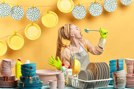 attractive awesome girl in gray apron using brush as a microphone in the kitchen with modern...