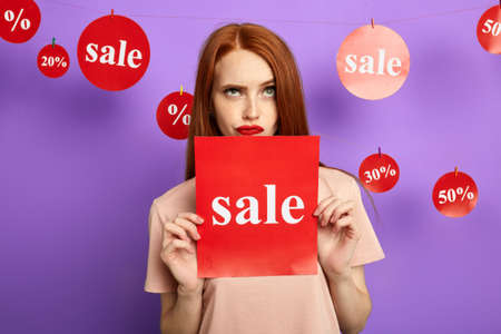 sad angry woman holding a card, girl isnt satisfied with sale. frustrated customer doesnt want to take part in the saleの写真素材